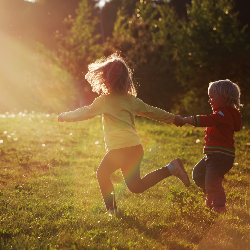 Two young children running and playing outdoors in a sunlit field, highlighting the importance of outdoor time for healthy visual development and myopia prevention.