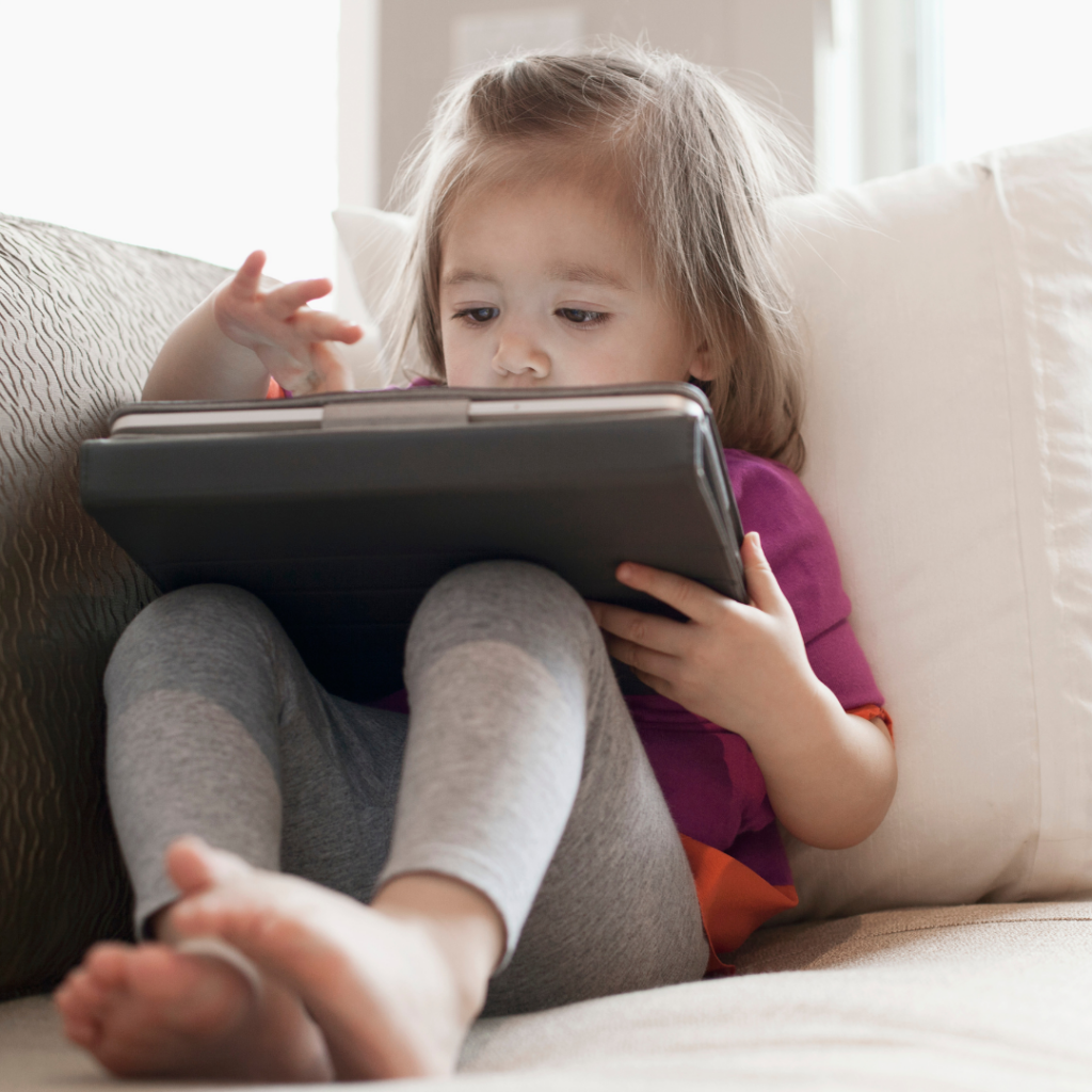 Young child sitting on a couch using a tablet device at close range, illustrating increased screen time and its connection to childhood myopia.