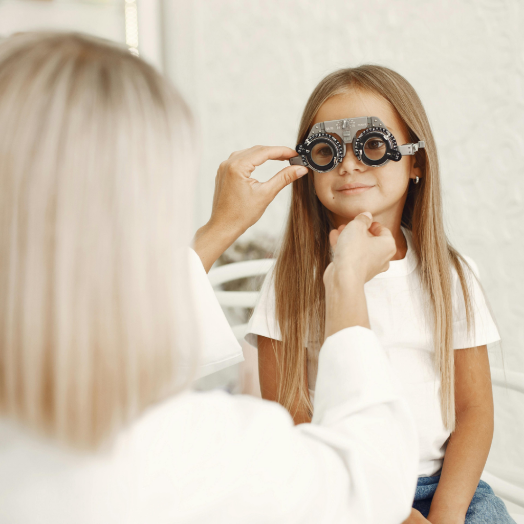 Child wearing a phoropter during a pediatric eye exam while an eye doctor adjusts the lenses to evaluate vision and monitor myopia progression.