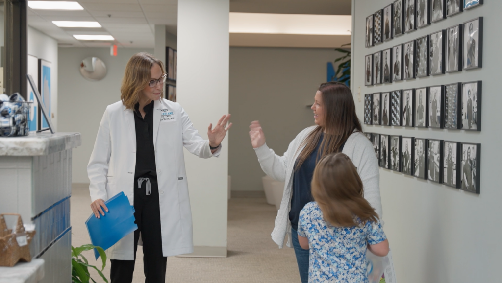 Eye doctor greeting a mother and child in a clinic hallway during a routine family eye exam visit.