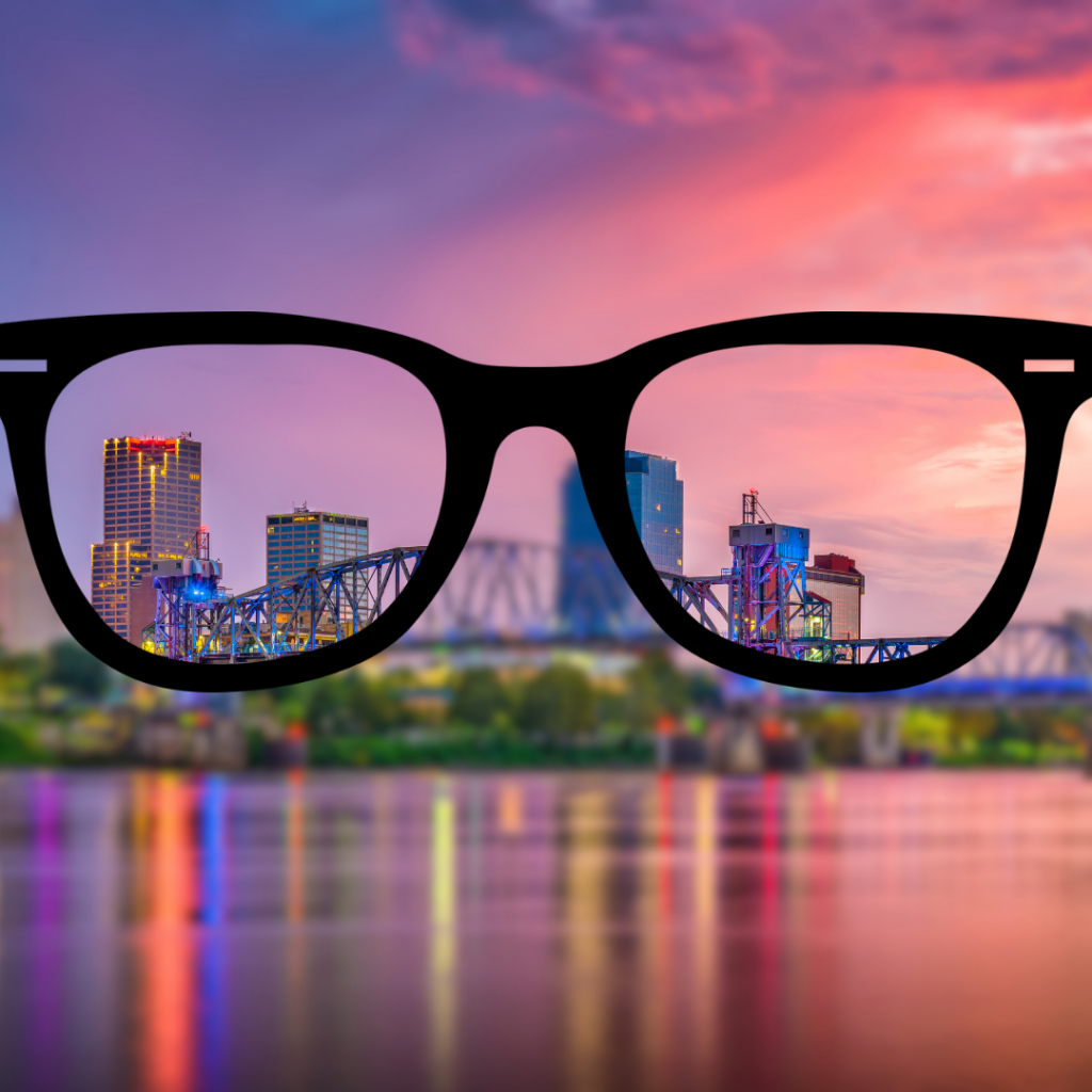 Black eyeglass frames overlooking the Little Rock skyline at sunset, with the city appearing clear through the lenses and blurred outside the frames to represent vision correction and myopia management.