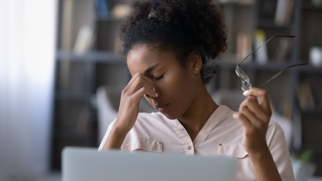 Woman experiencing digital eye strain and dry eye symptoms while using a laptop and holding eyeglasses during screen time.