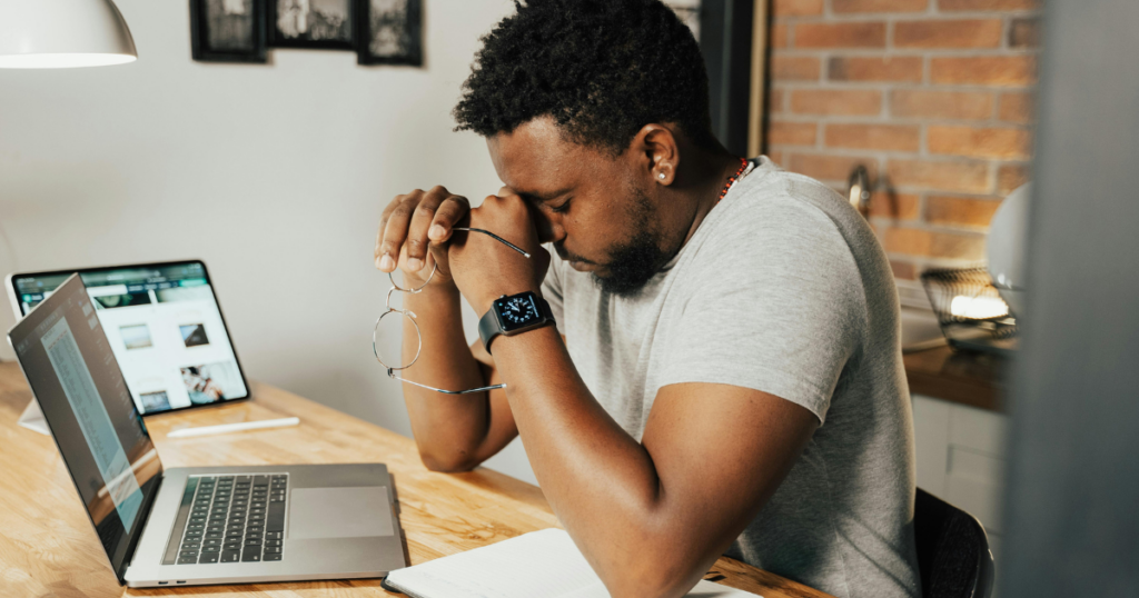 Man resting his eyes while working on a laptop and tablet.
