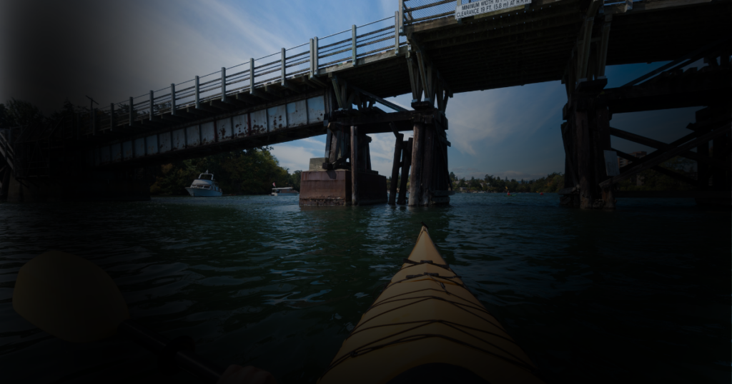 Simulation of severe peripheral vision loss while kayaking beneath a bridge, with the center visible and the surrounding scene darkened.