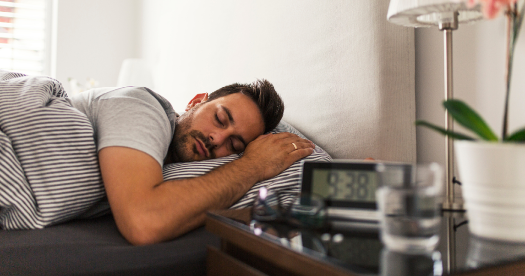 Man sleeping in bed beside a nightstand, illustrating the risks of sleeping while wearing contact lenses.